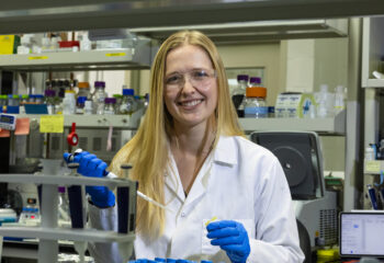 Scientist in a lab coat and gloves using a pipette in a laboratory setting.
