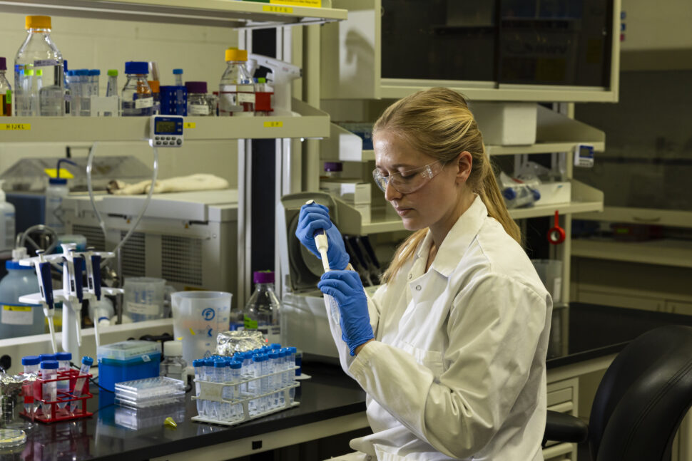 Scientist using a pipette to transfer liquid into a test tube at a laboratory bench.